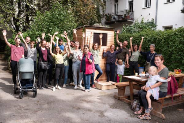 Impression vom Eröffnungsfest des ersten Wurmhotels in Wien im Planqzuadrat. Auf dem Bild sieht man die fröhliche Kompostgemeinchaft. Menschen allen Alters kommen im Innenhof der Wohnanlage zusammen und kompostieren gemeinsam mit dem hölzernen Wurmhotel.